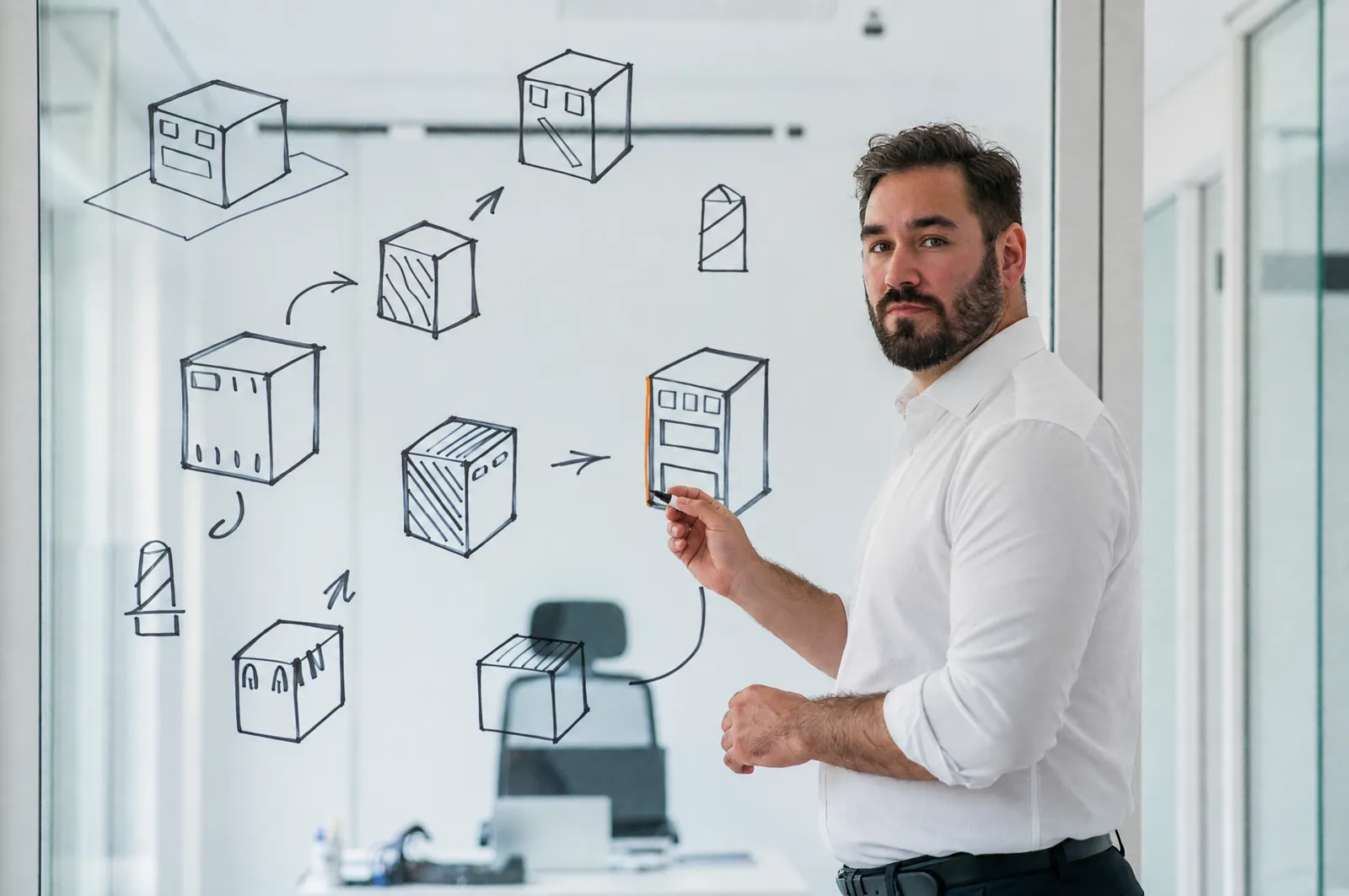 Ivo Schönberner in front of a glass wall with a hand-drawn IT architecture
